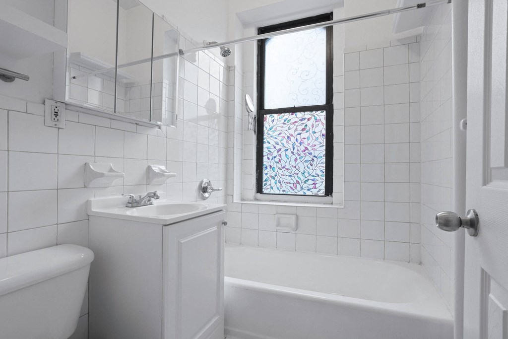a white bathroom with a tub and sink and a window