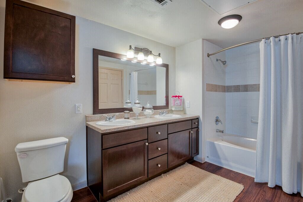bathroom with cabinets above toilet and below single sink with a big mirror and bathtub and lights on ceiling