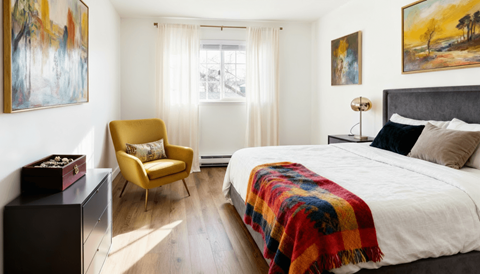 Twin Creek, Everett, WA, Apartments For Rent - Woodbrook - Bedroom With Vinyl Plank Flooring, Large Bed, Dresser, Armchair, Nightstand with Lamp, Insulated Windows, and Window Coverings.