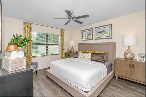 A bedroom with a bed, nightstand, and a plant.