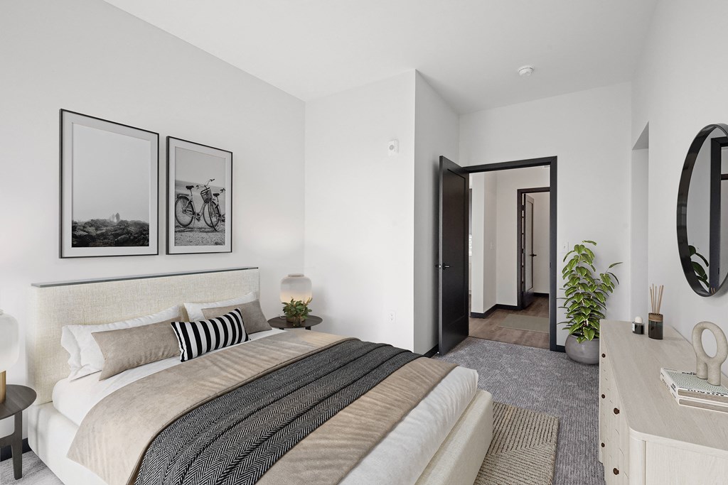 A bedroom with a large bed, a mirror, and two framed pictures on the wall.