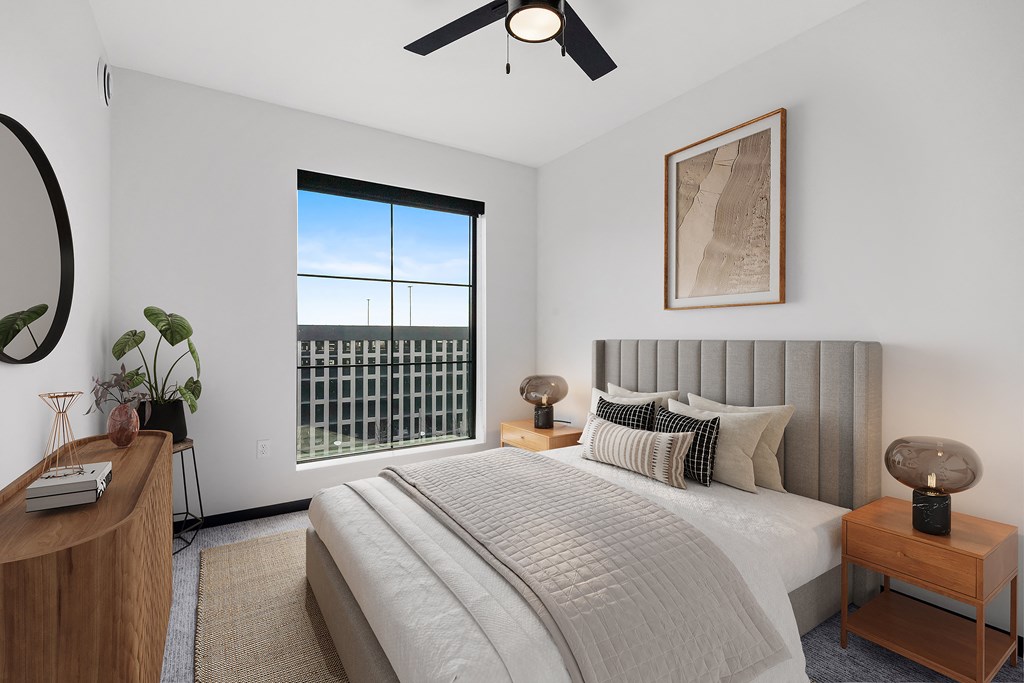 A bedroom with a large bed, a ceiling fan, and a window with a view of a fence.