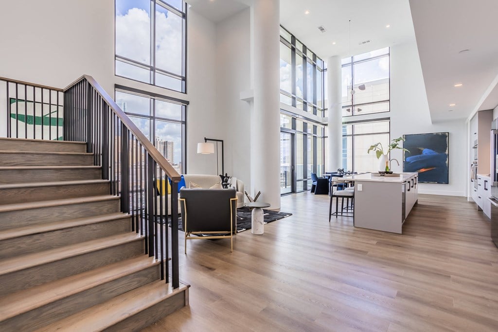 a living room with a staircase and a dining room with large windows