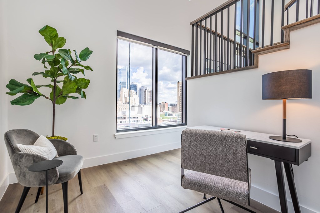 a living room with a large window and a desk with a chair and a lamp