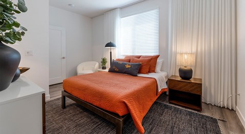 A bedroom with a bed covered in an orange blanket and a white chair.