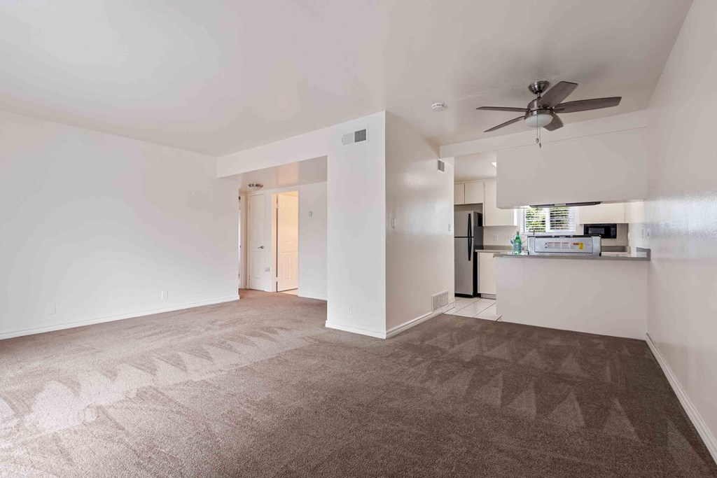 an empty living room with a ceiling fan and a kitchen