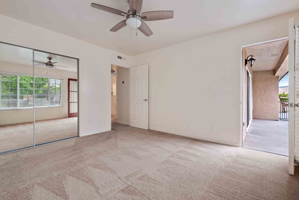 an empty living room with a ceiling fan and a mirrored closet