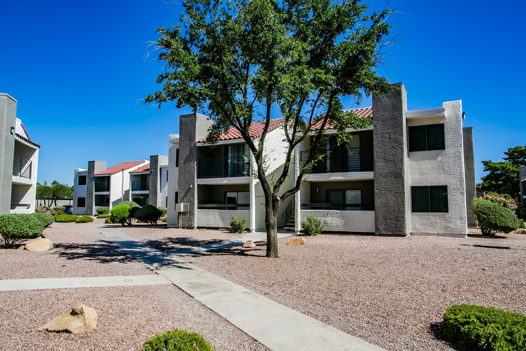an exterior view of an apartment building with a gravel courtyard and a tree