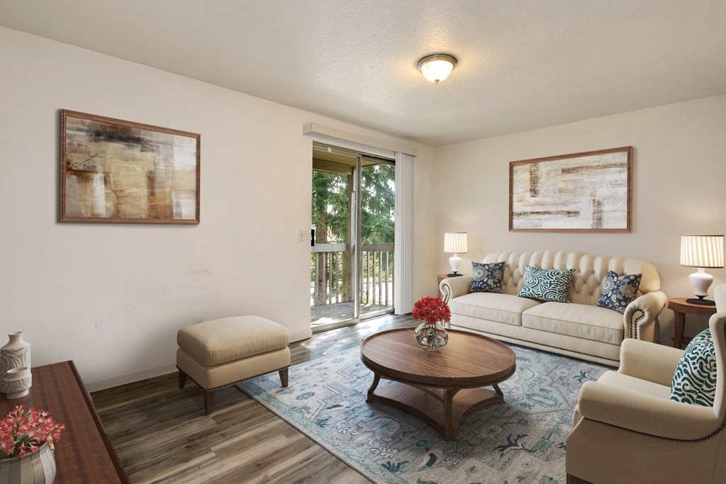 Lynnwood, WA, Apartments for Rent - Evergreen Grove - Living Room with Wood-Style Floor, Area Rug, Couch, Armchair, Stool, Round Coffee Table, Side Tables with Lamps, and Sliding Glass Door with Access to Patio.