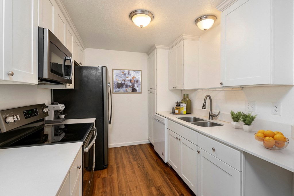 Apartments for Rent Lynnwood, WA - Evergreen Grove - Kitchen with Wood-Style Floor, White Cabinets, Range, Built-In Microwave, and Refrigerator.