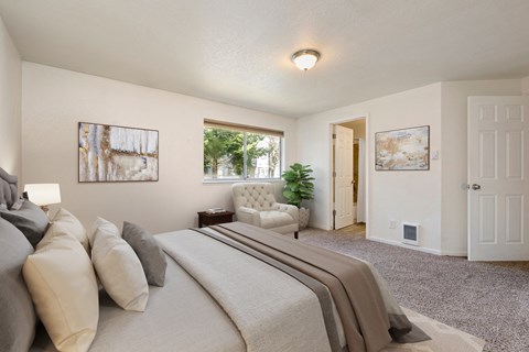 Lynnwood, WA, Apartments For Rent - Evergreen Grove Apartment Homes - Bedroom With Carpet Flooring, Bed, Couch, Side Table, Paintings, Lamp, And Large Windows.