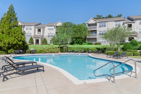 A swimming pool with a slide in the middle of a grassy area with chairs and a building in the background.