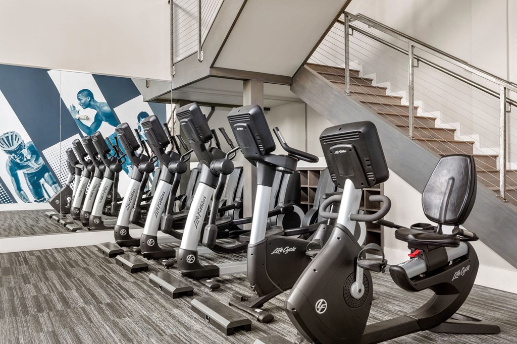 a row of exercise bikes in a fitness room with stairs