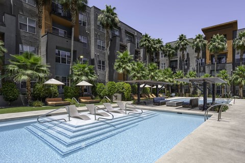 A swimming pool surrounded by lounge chairs and palm trees.