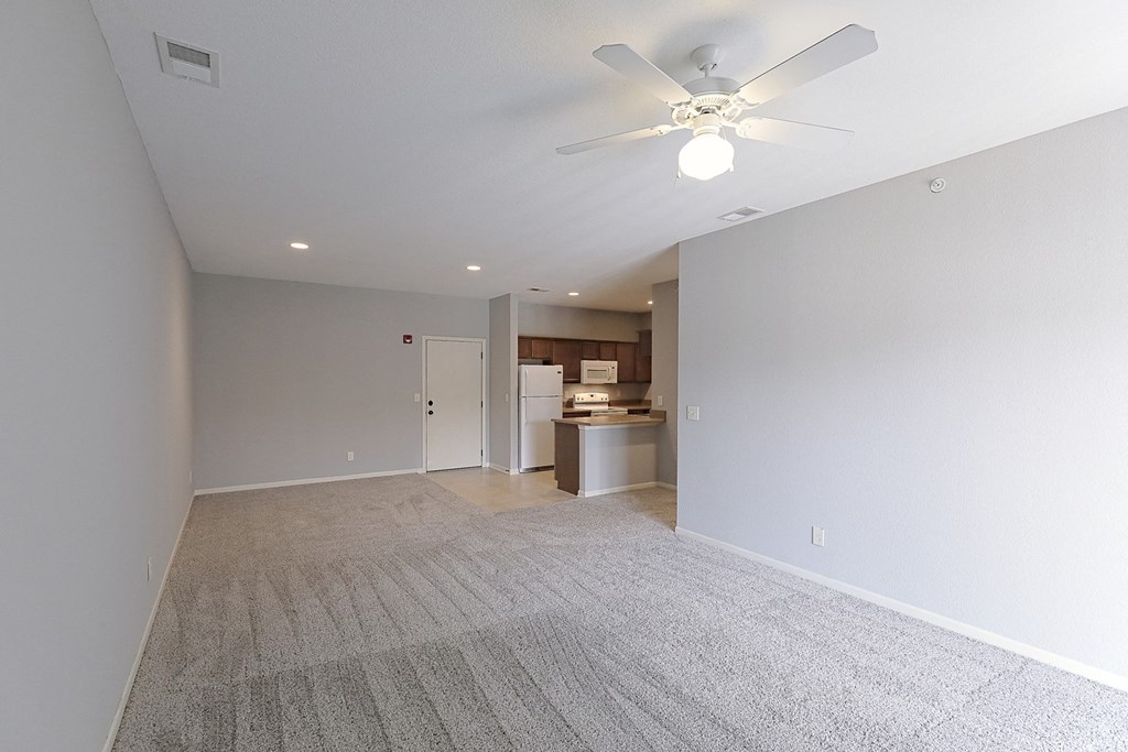 an empty living room with a ceiling fan and a kitchen