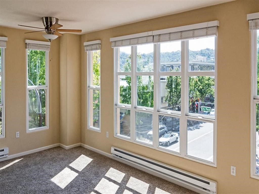 an empty living room with large windows and a ceiling fan