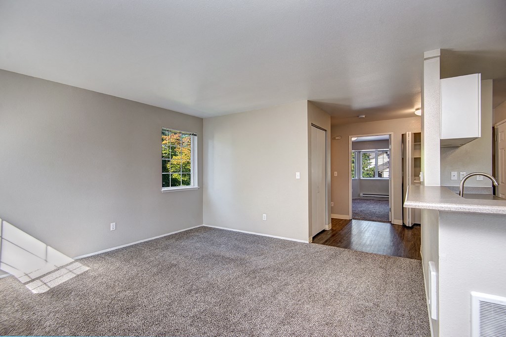an empty living room with carpet and a kitchen