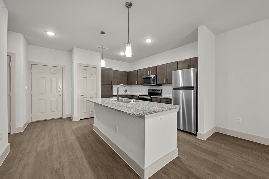 an empty kitchen with a marble counter top and a stainless steel refrigerator