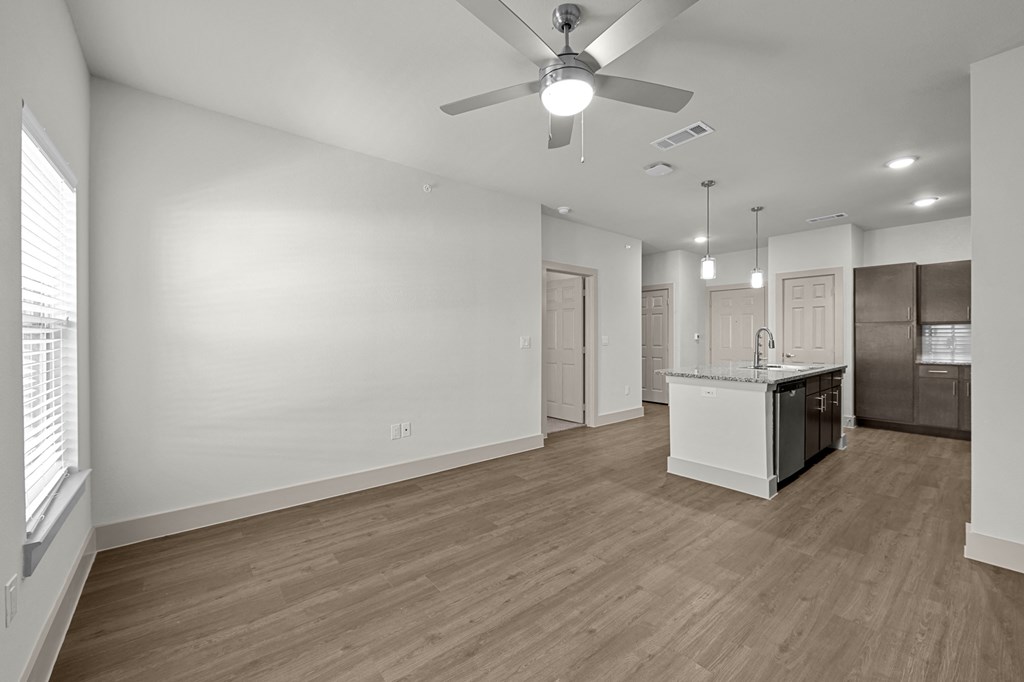 an empty living room with a kitchen and a ceiling fan