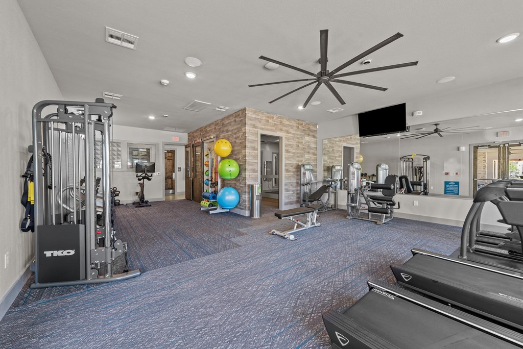 a gym with weights and cardio equipment and a ceiling fan