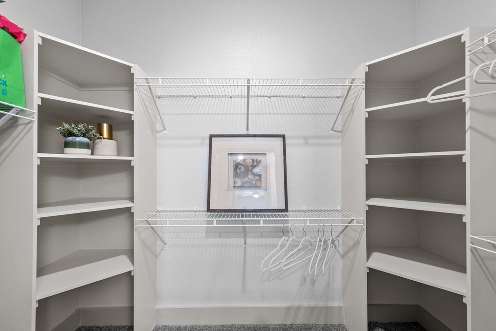 a walk in closet with white shelves and a picture on the wall