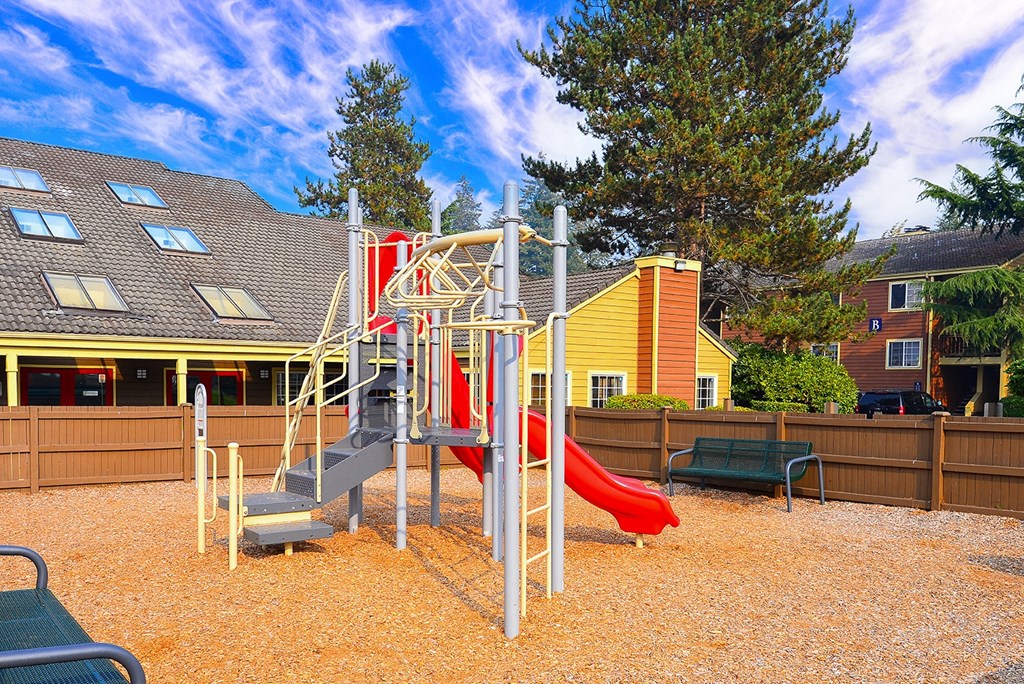 a playground with a red slide in front of a yellow house
