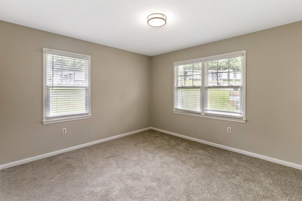 an empty bedroom with two windows and carpeting