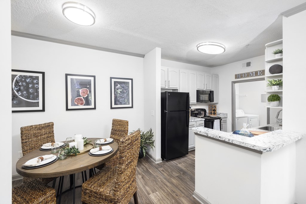 a dining area with a table and chairs and a kitchen in the background