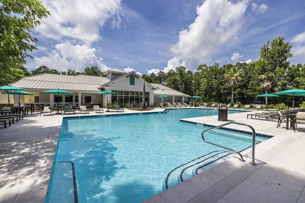 a large pool with lounge chairs and umbrellas in front of a building