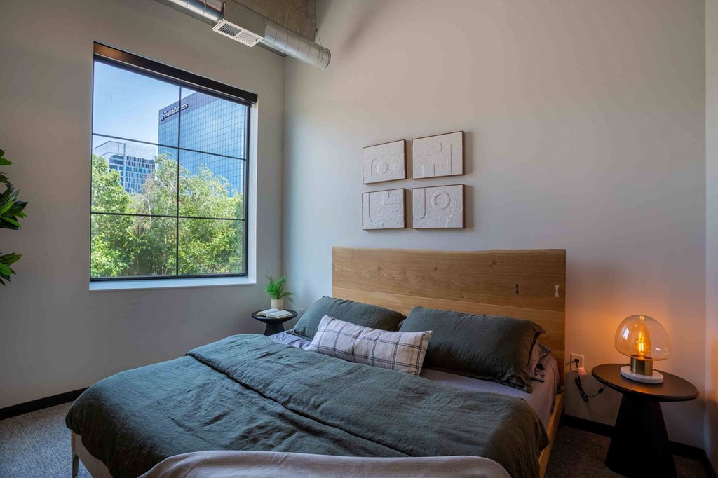 Bloomington, MN Apartments - Carbon31 - Bedroom with Large Window, Wall-to-wall Carpet, Large Bed, and Circular Nightstand