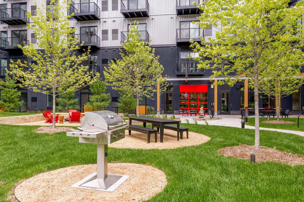 a picnic area with a grill and trees in front of an apartment building