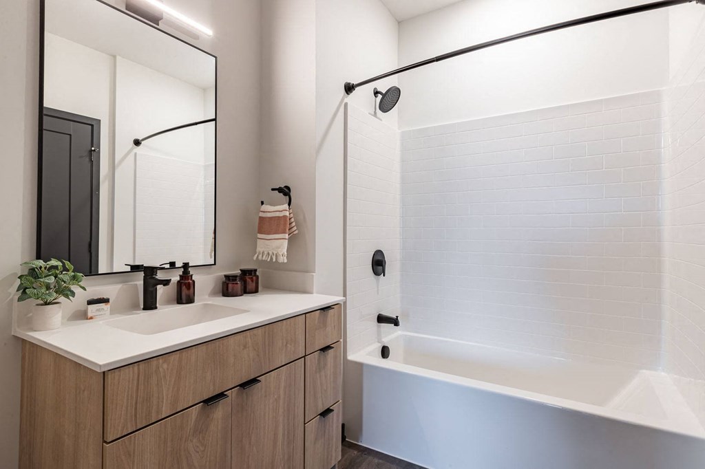 Bloomington, MN Apartments Near Mall of America - Carbon31 - Modern Bathroom with White Walls, Shower and Bathtub Combo, Sink, White Countertop, Black Plumbing Fixtures, and Large Mirror