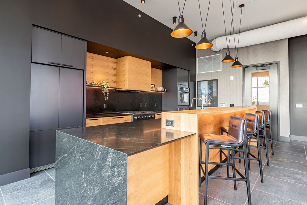 Apartments in Bloomington, MN for Rent - Carbon31 - Kitchen with Contrasting Black and Wooden Tones, Quartz Countertops, a Large Island with Bar Chairs, and Pendant Lights