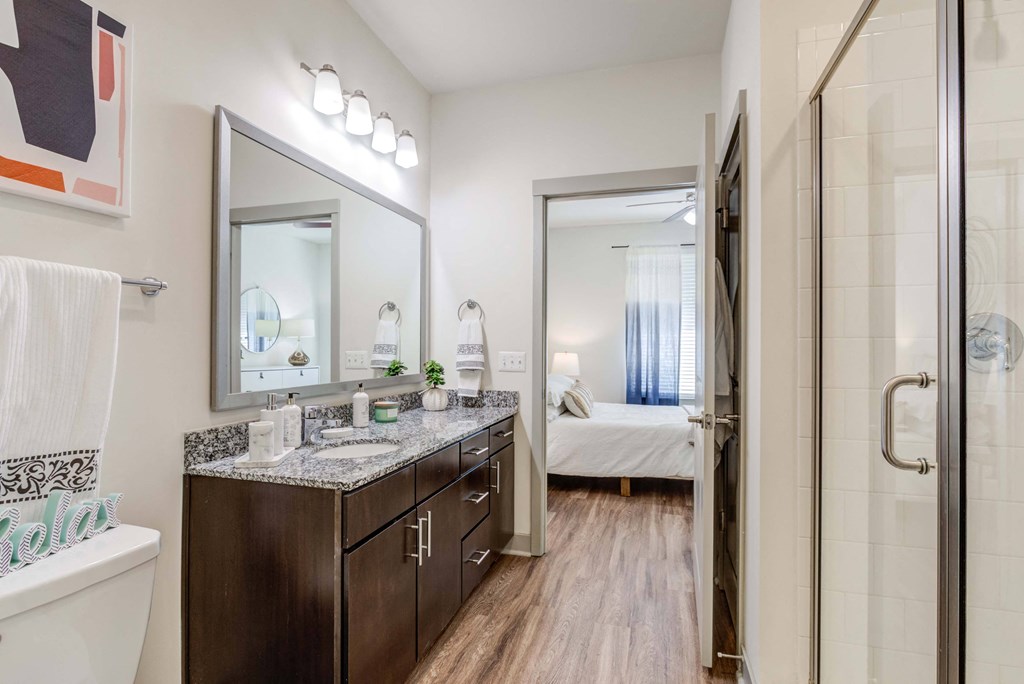 Modern bathroom with granite countertop, dark wood cabinets, and view into bedroom.