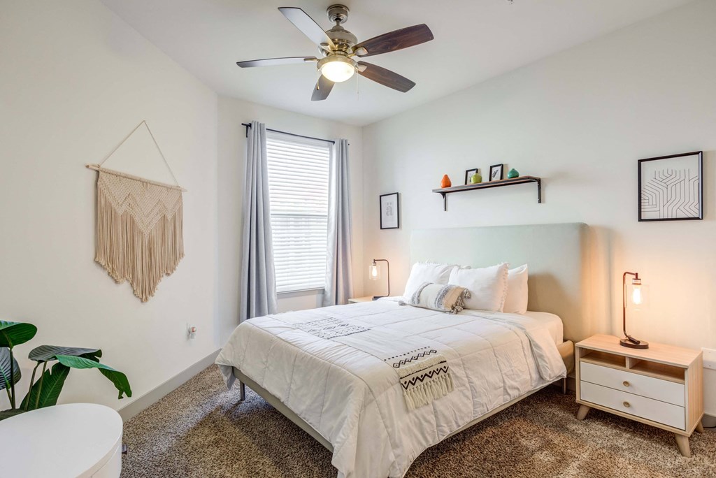 Bright, modern bedroom with queen bed, macrame wall hanging, and ceiling fan.