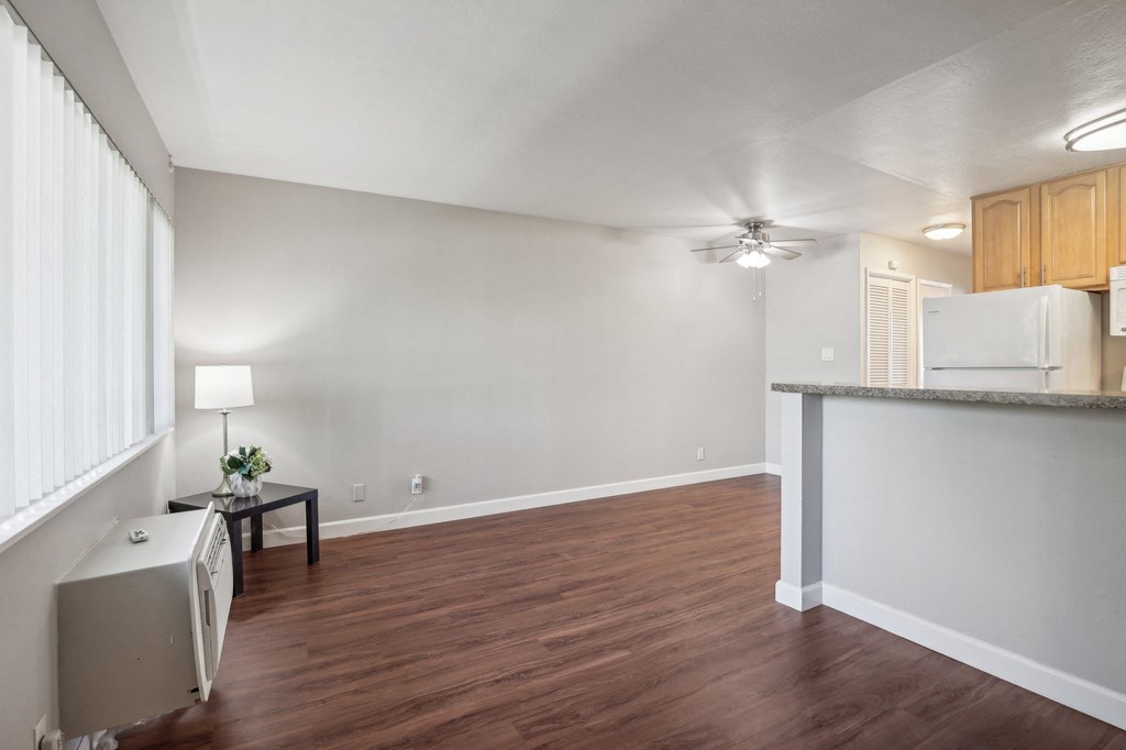an empty living room with a kitchen and a ceiling fan