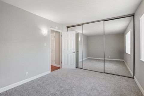 2-Bedroom Apartments in Downtown Walnut Creek, CA - Carmel House Apartments - Bedroom With Gray Walls, Carpeted Flooring, Mirrored Closet Doors, Open Entry Door, And Natural Light From Two Windows.
