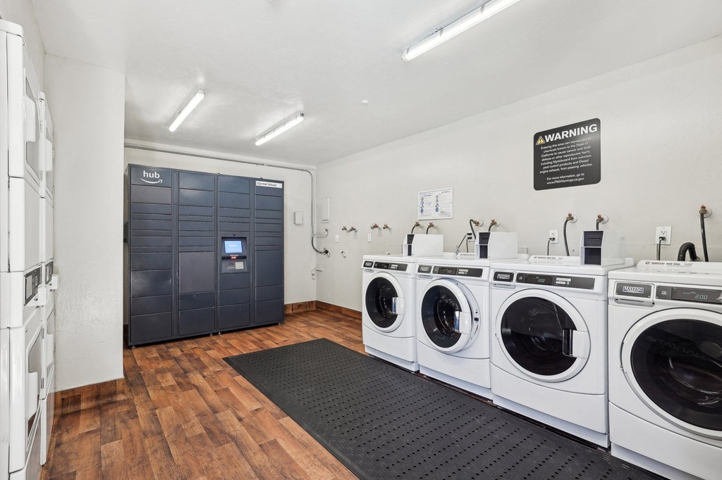 Downtown Walnut Creek, CA Apartments for Rent - Carmel House - Laundry Facility with Wood-Inspired Flooring, Floor Mat, Washers, Dryers, and Amazon Hub Package Lockers.