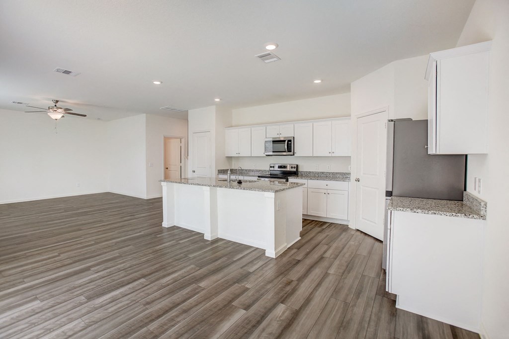 an open kitchen and living room with white cabinets and stainless steel appliances