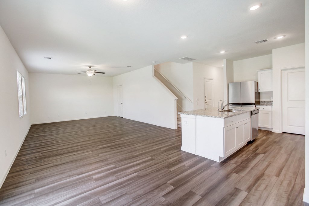 an empty living room with a kitchen and a staircase