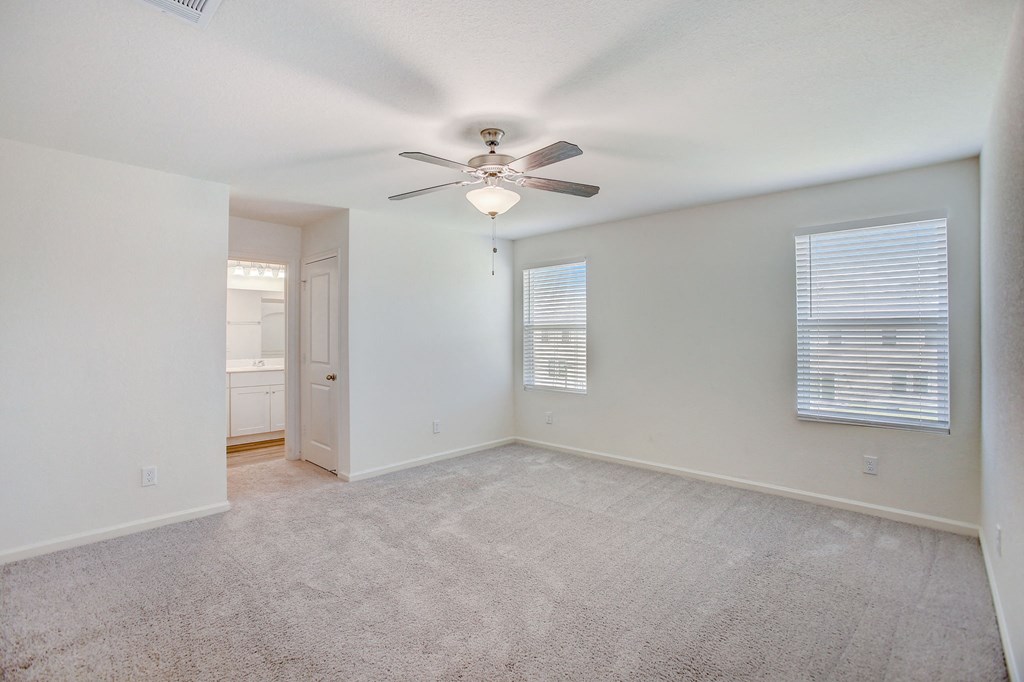 an empty living room with a ceiling fan and a door to a bathroom