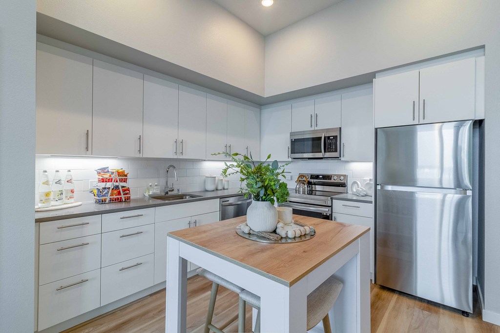 a white kitchen with stainless steel appliances and a wooden table