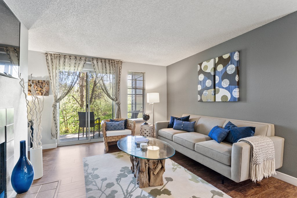A living room with a couch, coffee table, and a large window with curtains. at Cedar Crest, Beaverton