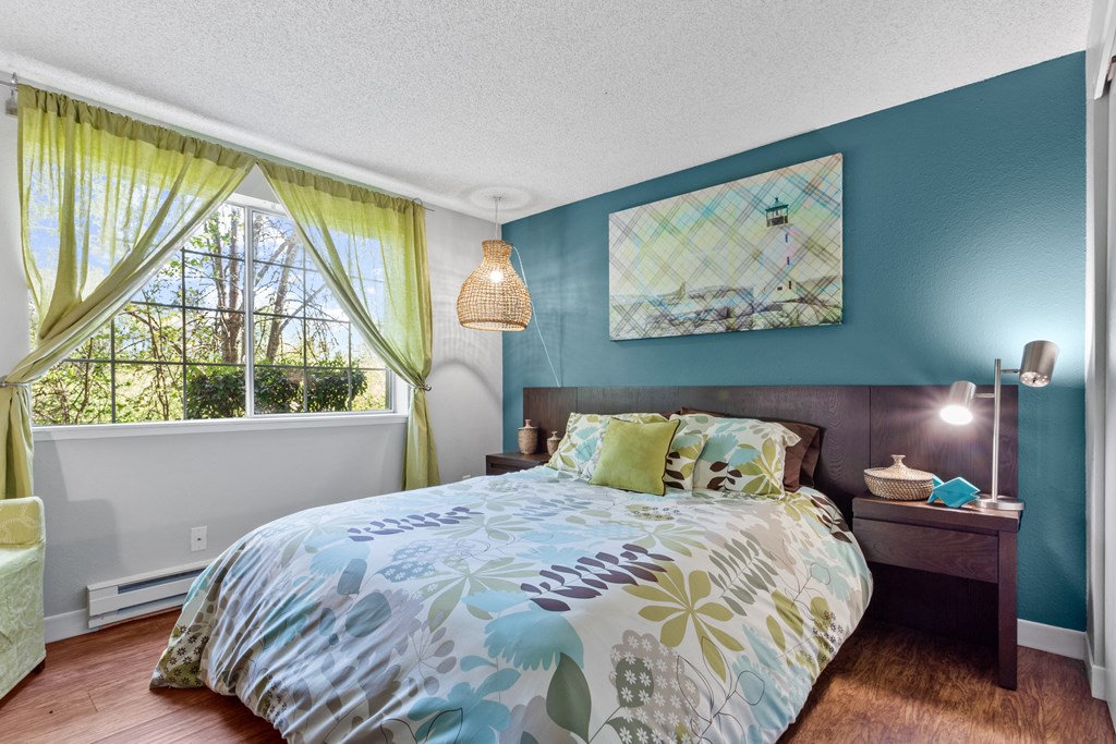 A bedroom with a bed, nightstand, and window with curtains. at Cedar Crest, Beaverton