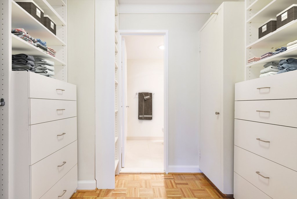 A hallway with white cabinets and drawers on both sides leading to a bathroom.