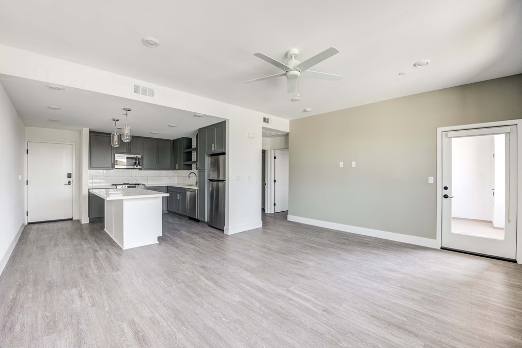 an empty living room with a kitchen and a ceiling fan