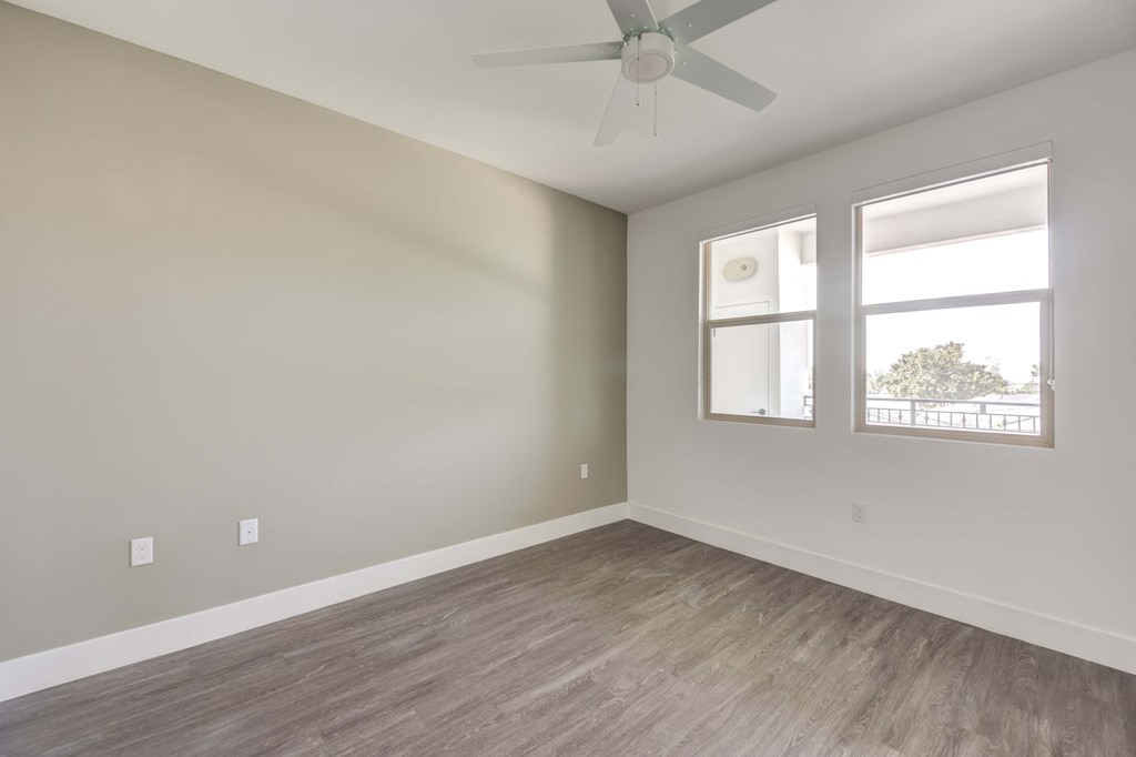 an empty room with a ceiling fan and two windows