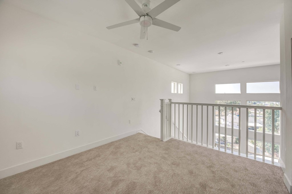an empty living room with a ceiling fan and a balcony