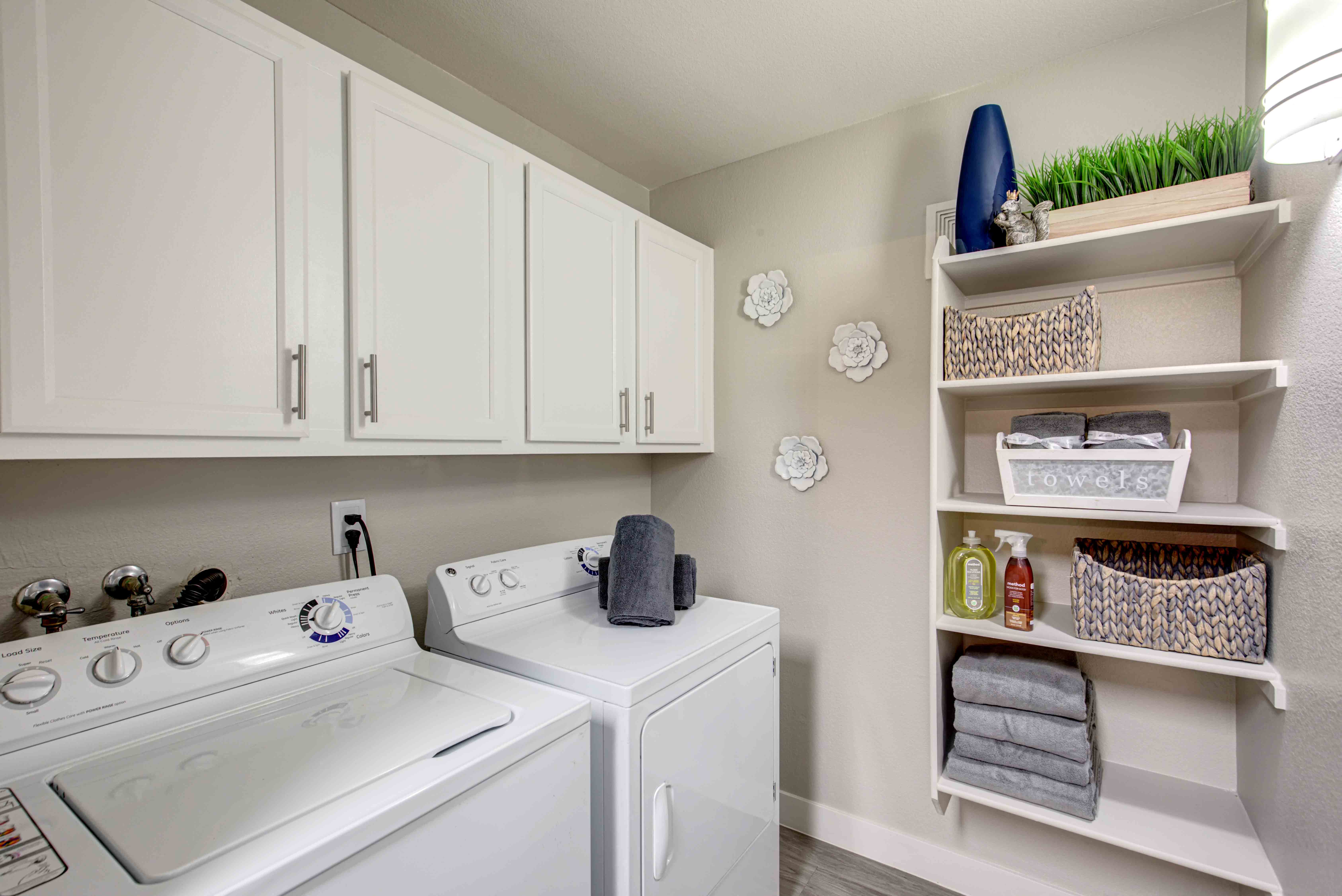 Las Vegas, NV Apartments - Cimarron -  Laundry Room with In-Unit Washer and Dryer, Resilient Wood-Style Flooring, and Storage Cabinets and Shelves