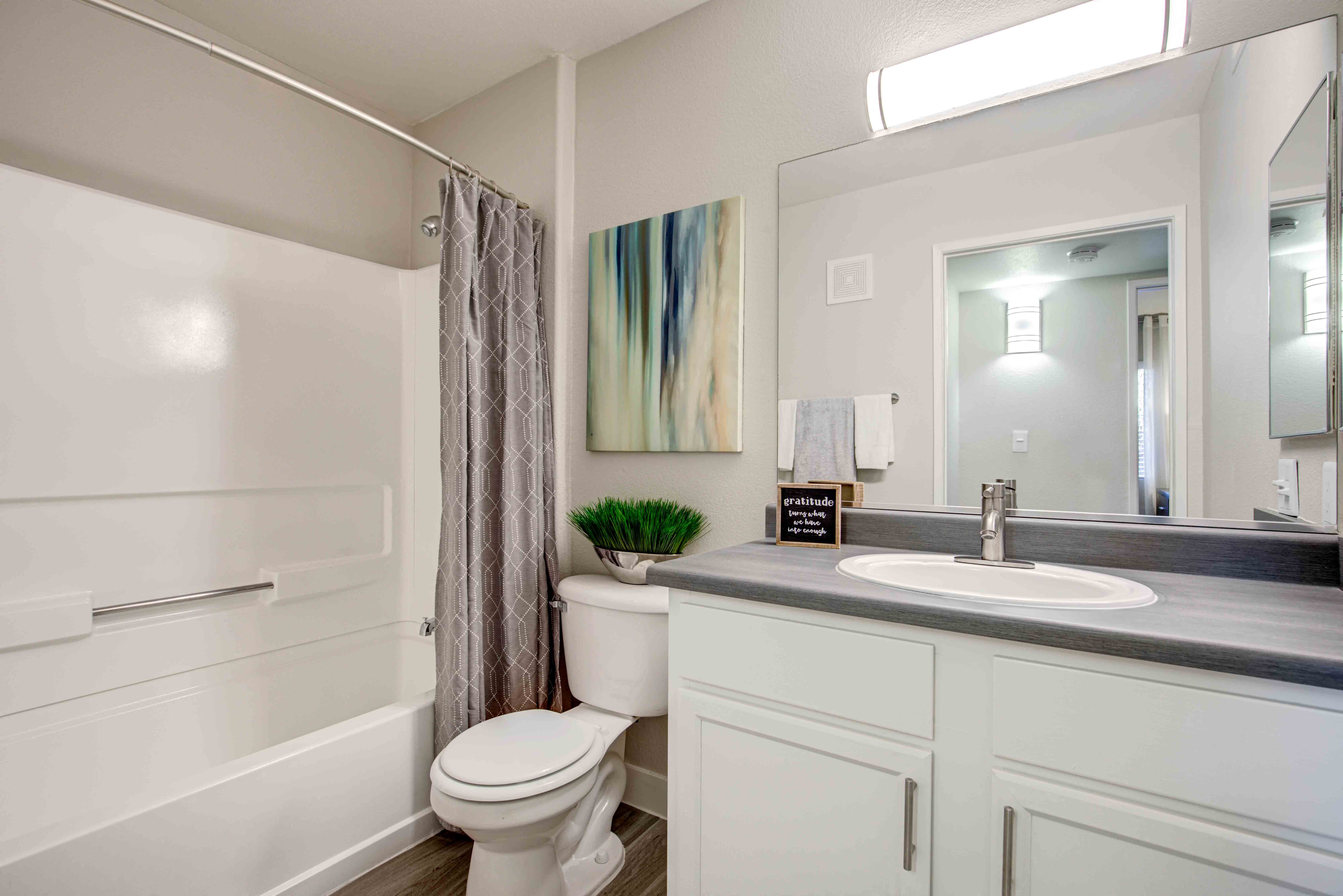 Newly Renovated Apartments in Las Vegas, Nevada - Cimarron - Bathroom with Large Vanity, Grey Counters, White Cabinets, Resilient Wood-Style Flooring, a Shower, and a Bathtub